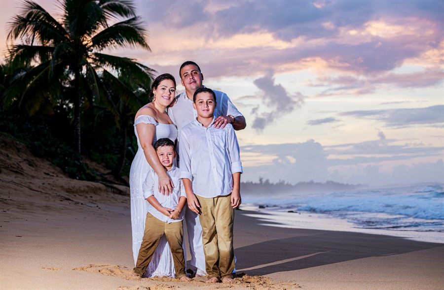 Family posing on a palm-lined beach at sunset