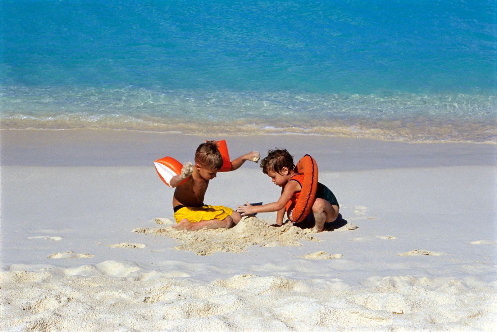 Two young children building in white sand, the fun of cheap cruises for families